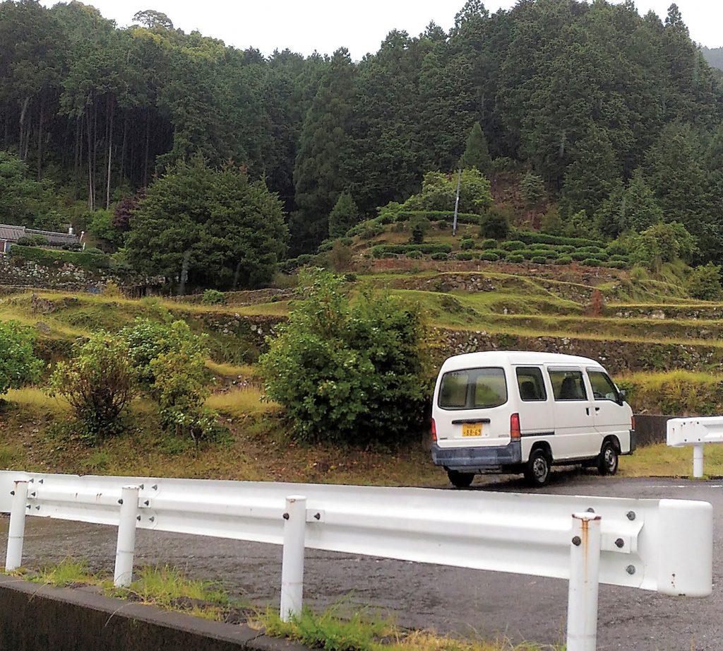 色川地区の風景。段々畑のある山都里に１台の車が停車している。